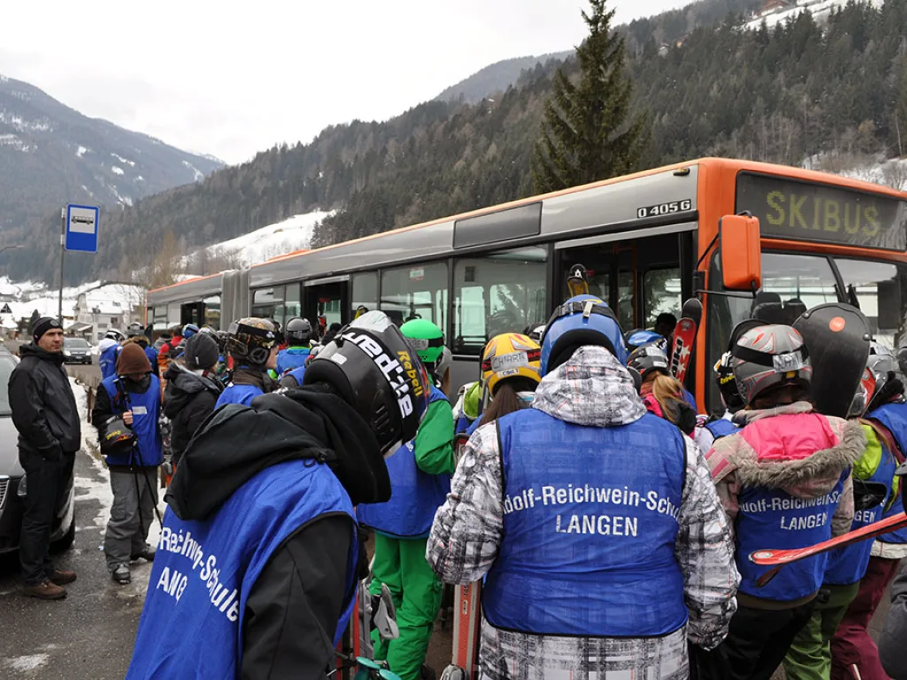 Jugendliche mit Skiausrüstung steigen an der Haltestelle in den Skibus.